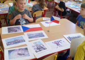 Dzieci siedzące przy stoliku z flagą Czech i obrazkami związanymi z Czechami.